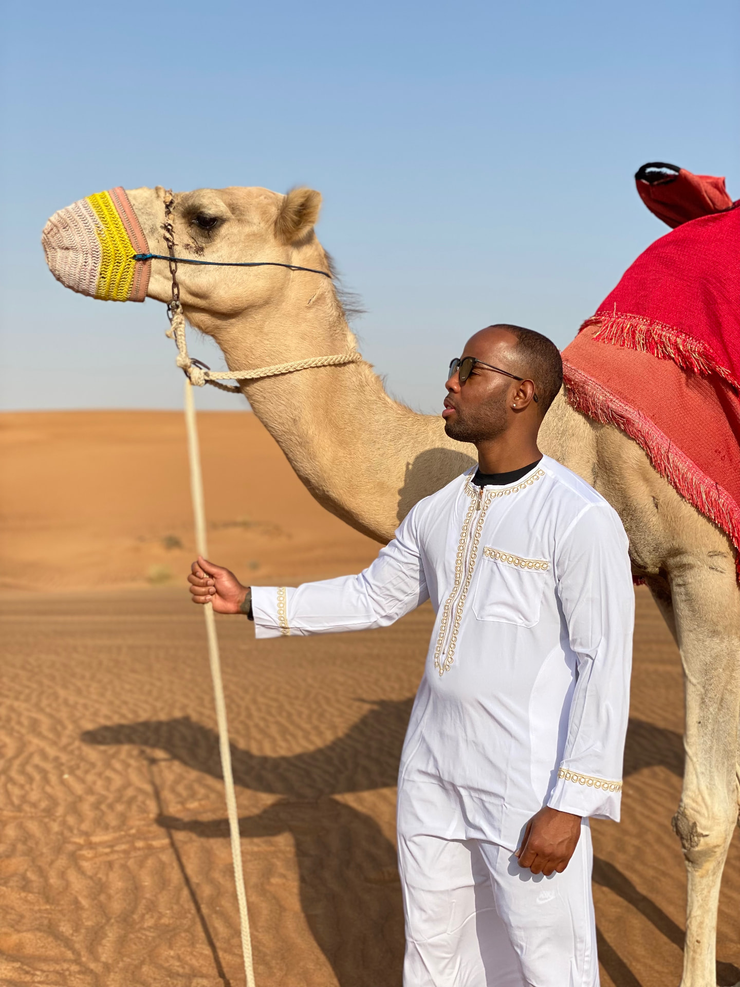 A traveler in white traditional attire beside a camel in the desert